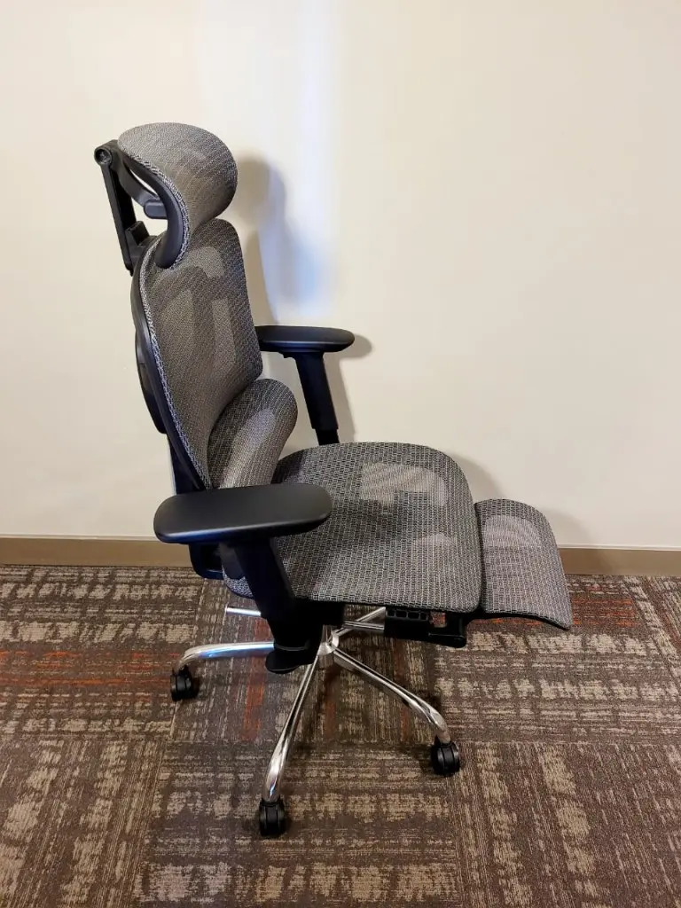 A mesh office chair with an extended footrest, adjustable arms and a chrome base.