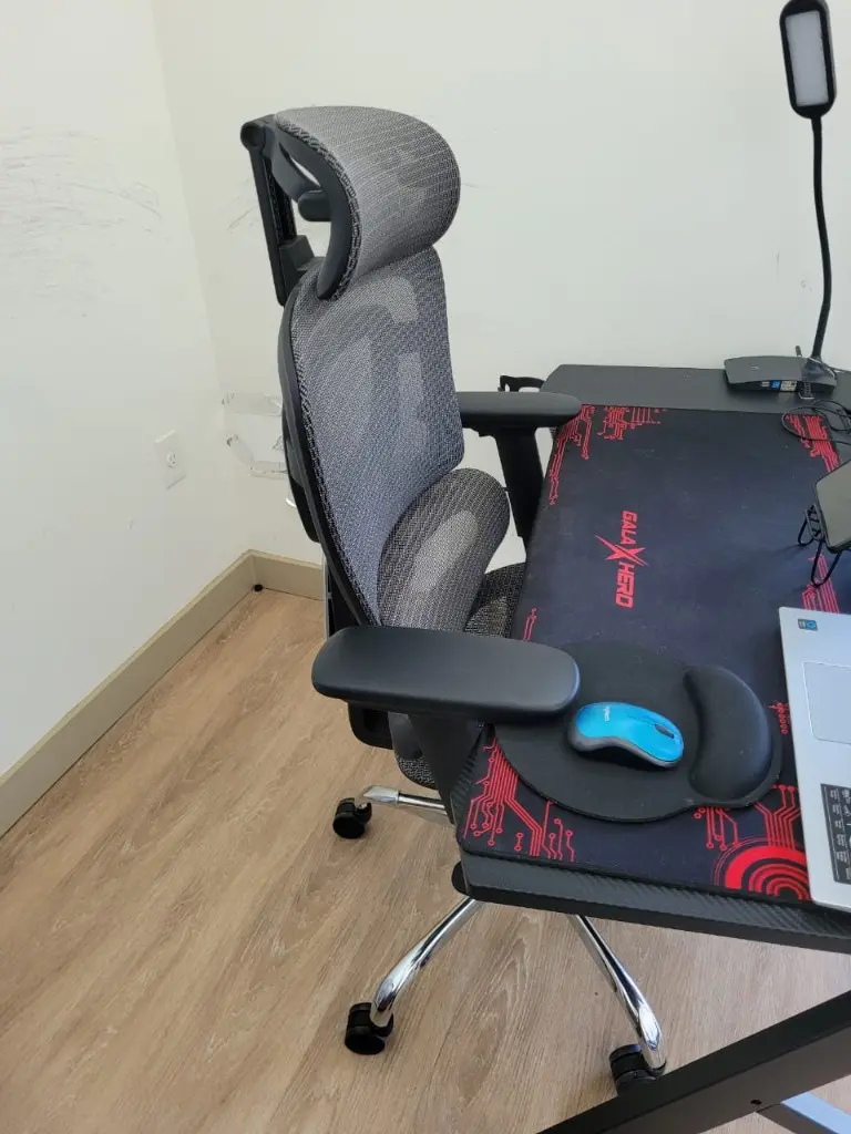 Side view of a mesh office chair at a desk, with a lumbar cushion, wrist rest and mouse.