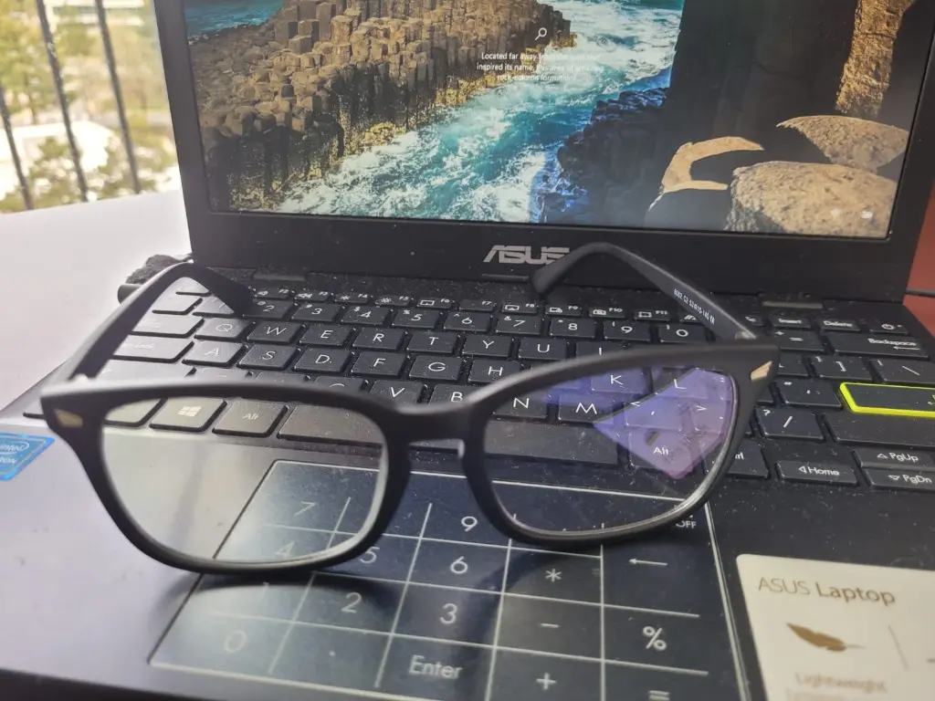 A pair of screen glasses resting on an open laptop keyboard.